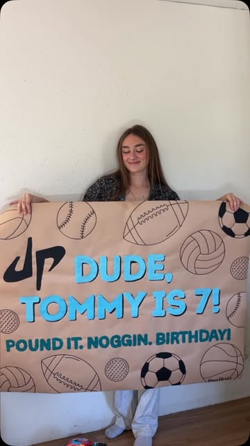 Ella holding a Dude, Tommy is 7 sports birthday banner